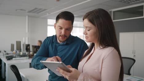 Professional-young-businessman-and-businesswoman-discussing-work-together-on-digital-tablet-in-modern-office