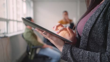 Close-up-of-businesswoman-working-on-digital-tablet-while-her-colleagues-communicating-on-the-background-in-the-office