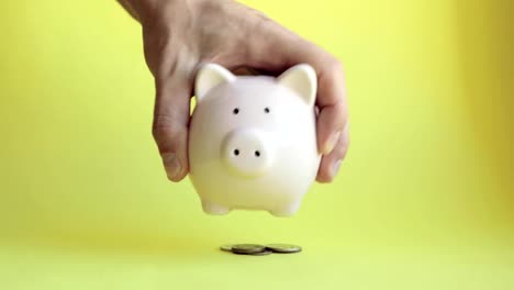 Man-shaking-piggy-bank-of-pig-shape-and-coins-fall-out-on-yellow-background