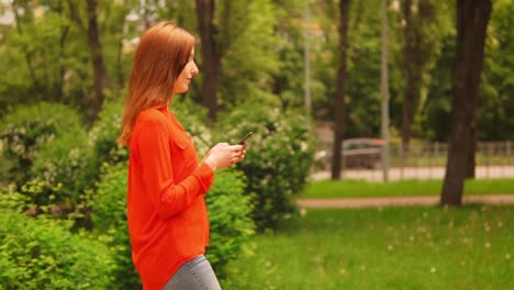 Seitenansicht-Ingwer-Frau-zu-Fuß-auf-der-Straße-halten-Smartphone