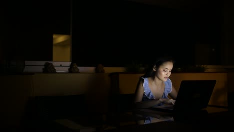 Joven-mujer-asiática-feliz-usando-el-ordenador-portátil-en-la-habitación-oscura