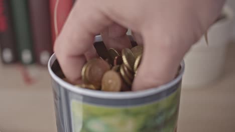 Male-hand-takes-a-handful-of-euro-coins-and-bank-note-from-a-jar