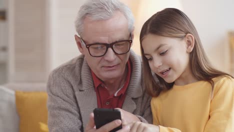 Chica-caucásica-de-10-años-enseñando-abuelo-cómo-usar-el-teléfono-inteligente