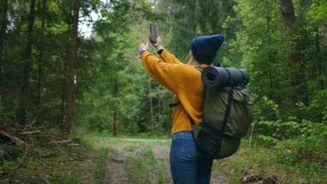 Slow-motion:-Young-woman-hiker-using-her-smart-phone-while-enjoying-her-weekend-in-forest.-Traveling-woman-with-backpack-walking-on-path-the-forest-looking-at-the-telephone-and-map-in-green-wood