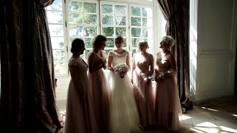 Bridesmaids-laughing-happy-near-bride-slow-motion.-Beautiful-girlfriends-pose-surrounding-bride-amusing-and-talking-in-sun-light-room.-Bachelorette-party-emotional.-Elegant-wedding-dress-fashion-style