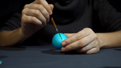 Female-hands-painting-the-egg-decoration-for-easter-over-a-gray-background.