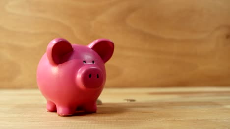 Coins-falling-into-piggy-bank-against-wooden-background