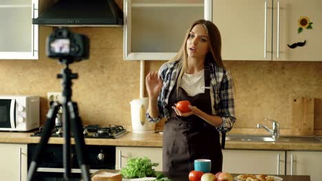 Young-attractive-woman-in-apron-shooting-video-food-blog-about-cooking-on-dslr-camera-in-kitchen