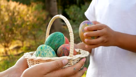 Close-up-of-woman-hand-holding-a-basket-with-easter-eggs.-Children-put-eggs-into-basket-in-sunshine-background