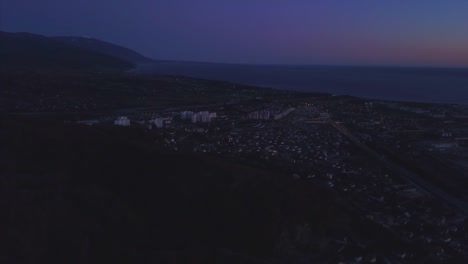 Panorama-nocturno-de-la-ciudad-de-Sochi-a-vista-de-pájaro.-Clip.-Panorama-de-Sochi-desde-el-aire.-Casas,-calles,-árboles,-la-noche-en-el-cielo-son-visibles.-En-la-distancia-se-puede-ver-el-mar.-Sochi,-Rusia