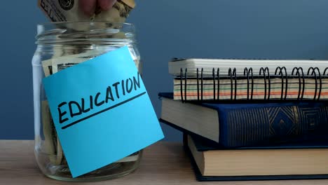 Hand-putting-dollar-bills-in-jar-with-label-education.-Money-for-college.