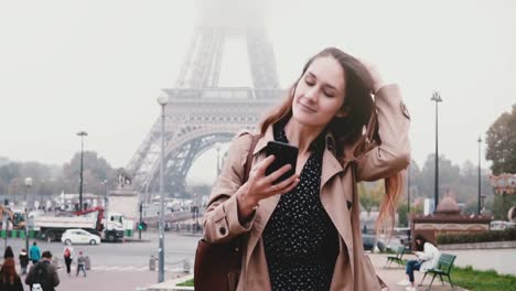 Joven-hermosa-mujer-caminando-cerca-de-la-Torre-Eiffel-en-París,-Francia-y-usando-el-teléfono-inteligente,-navegar-por-Internet