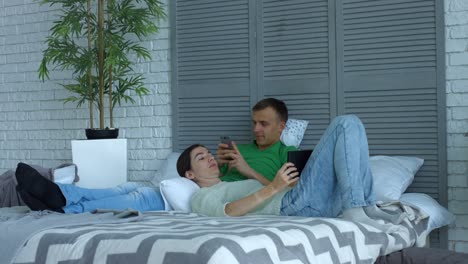 Loving-couple-with-digital-devices-relaxing-on-bed