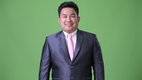 Young-handsome-overweight-Asian-businessman-against-green-background