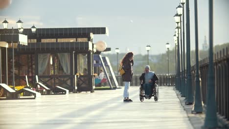 Hombre-discapacitado-en-silla-de-ruedas-hablar-por-teléfono,-caminar-juntos-a-su-novia-en-el-muelle