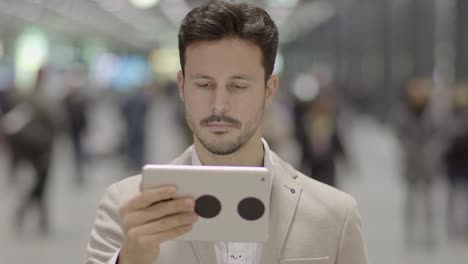 Guapo-joven-empresario-escribiendo-textos-sobre-tableta-digital-en-el-espacio-público