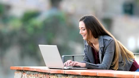 Glückliche-Frau-Eingabe-auf-einem-Laptop-in-einem-Balkon