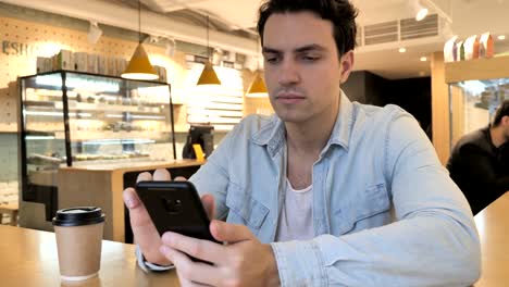 Young-Man-Typing-Message-in-Cafe,-Browsing-on-Phone