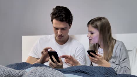 Young-Couple-Sharing-Information-while-Using-Smartphone-in-Bed