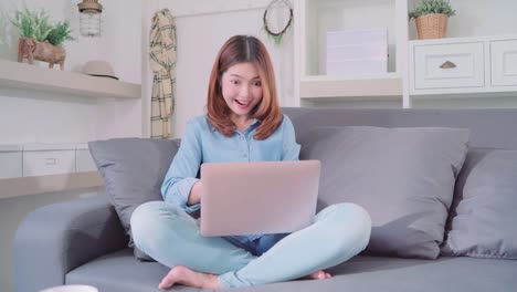 Portrait-of-beautiful-attractive-young-smiling-Asian-woman-using-computer-or-laptop-while-lying-on-the-sofa-when-relax-in-living-room-at-home.-Enjoying-time-lifestyle-women-at-home-concept.