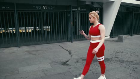 Plus-size-blond-mixed-racee-smiling-woman-wearing-red-sportswear-using-smartphone-outdoors