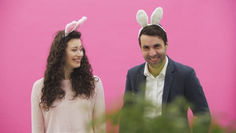 Young-couple-standing-on-pink-background.-During-this-time,-they-look-at-the-camera-together,-talking.-Sincerely-smile.