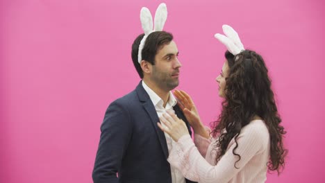 Young-couple-standing-standing-on-pink-background.-During-this,-they-carry-out-the-movement-of-rabbits.-The-woman-put-her-hands-on-his-neck,-choking.-After-this,-you-are-genuinely-laughing.