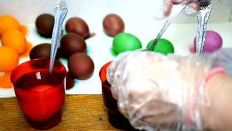 Woman-paints-Easter-eggs-in-different-colors,-dipping-them-into-cups-with-multicolored-dyes.