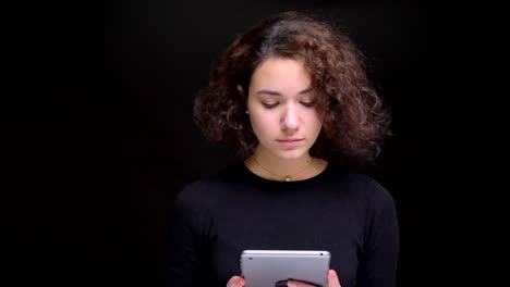 Retrato-en-primer-plano-de-joven-atractiva-mujer-caucásica-con-pelo-rizado-usando-la-tableta-en-frente-de-la-cámara