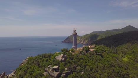 Drone-view-light-house-on-green-mountains-and-blue-sea-on-clear-horizon.-Aerial-view-sea-lighthouse-on-mountain-cliff-and-blue-sky-landscape