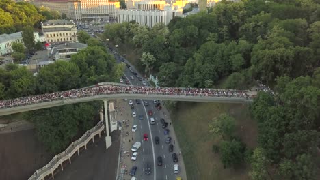 Eine-Menschenmenge-auf-einer-Fußgängerbrücke-ist-am-Frühlingsabend-zu-sehen.-Luftaufnahme.-Eine-neue-Fahrrad-Fußgängerbrücke-im-Zentrum-der-Hauptstadt-der-Ukraine,-der-Stadt-Kiew.-Ausflüge-und-Spaziergänge-für-Touristen