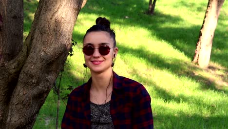 Beautiful-girl-in-sunglasses,-actively-laughing,-and-showing-thumb-up-while-sitting-on-a-bench-in-the-park