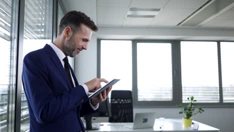 Glücklicher-Geschäftsmann-arbeitet-im-Büro-mit-Tablet