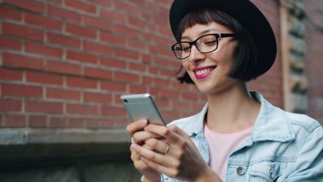 Lento-movimiento-de-mujer-alegre-usando-teléfono-inteligente-moderno-caminando-al-aire-libre-en-la-ciudad