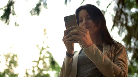 Joven-morena-mujer-escribiendo-mensajes-en-el-chat-público-en-la-red-social-al-aire-libre-en-el-bosque