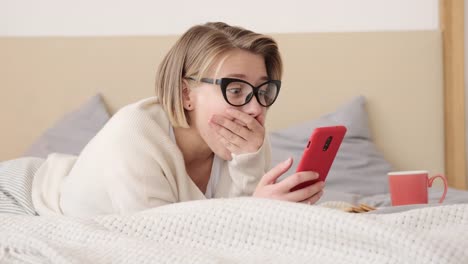 Schockierte-junge-Frau,-die-auf-Handy-im-Bett-schaut