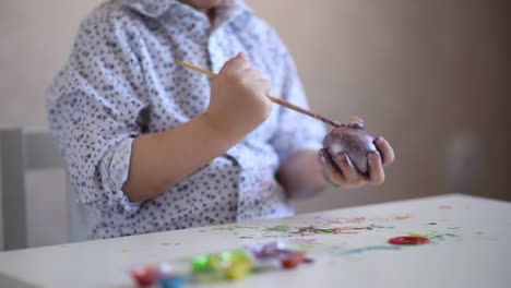 The-hands-of-a-litlle-child-with-a-brush-paint-an-Easter-egg-in-violet-color-on-the-table.