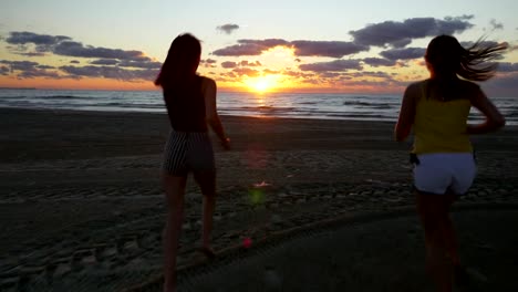 Girl-friends-running-on-the-beach-towards-the-sea-at-sunrise