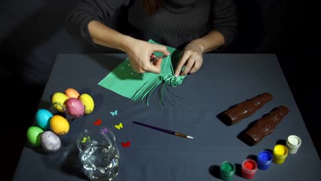 Female-hands-curl-fringe-of-the-green-paper-with-metal-scissors-over-gray-table