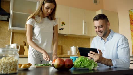 Atractiva-pareja-charlando-en-la-cocina-temprano-en-la-mañana.-Hermosa-mujer-alimenta-a-su-marido-mientras-se-cocina-el-desayuno