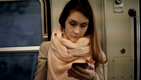 Joven-atractivo-de-pie-en-el-metro-y-con-el-smartphone.-Mujer-morena,-navegar-por-Internet-en-tren