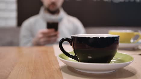 Eine-nicht-erkennbare-Mann-sitzt-im-Restaurant-und-nutzen-das-Smartphone-in-die-Unschärfe-von-einer-Tasse-Tee.-Slow-motion