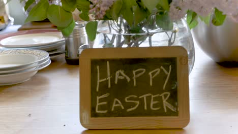 Frohe-Ostern,-geschrieben-auf-einer-kleinen-Tafel-gegen-eine-Vase-mit-schönen-Blumen