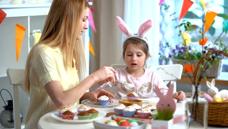 Joven-madre-y-su-hija-con-orejas-de-conejo-cocinar-cupcakes-de-Pascua