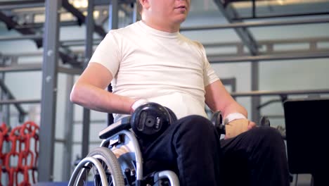 A-disabled-man-is-sitting-in-a-wheelchair-with-dumb-bells,-moving-his-shoulders-and-talking