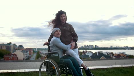 Portrait-of-a-happy-disabled-man-in-a-wheelchair-embraces-with-young-woman-outdoors