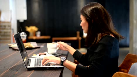 Asian-woman-working-on-laptop-and-drinking-coffee-in-cafe