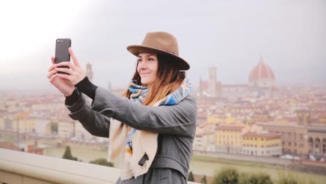 Happy-smiling-tourist-girl-taking-smartphone-selfie-photo-at-amazing-cityscape-panorama-of-autumn-foggy-Florence,-Italy.