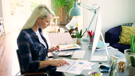 Attractive-Blond-Businesswoman-Calculating-Finances-In-Home-Office