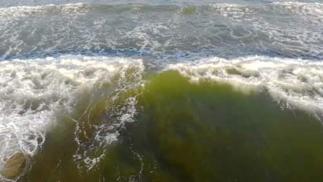 Las-olas-del-mar-Mediterráneo-vienen-a-la-costa,-la-cámara-sube-lentamente-y-muestra-la-ciudad-de-Valencia